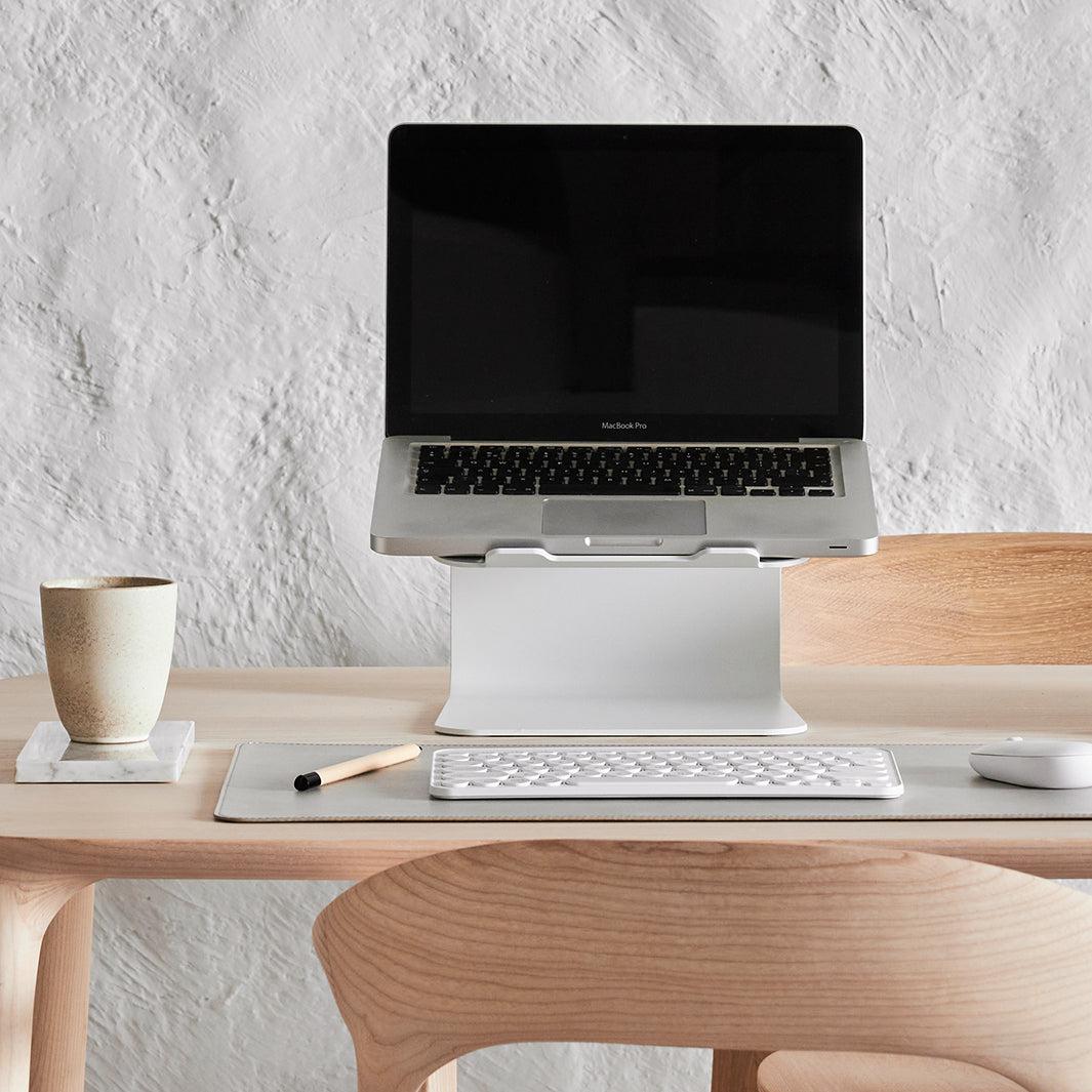 Werkplek met laptop open op witte standaard onderlegger in stone en witte accessoires
