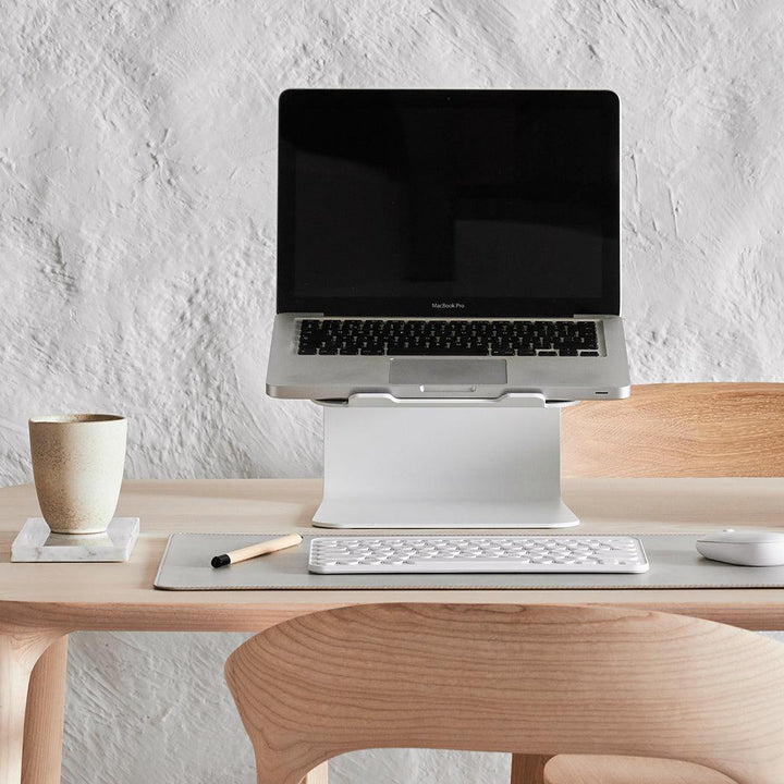 Werkplek met laptop open op witte standaard onderlegger in stone en witte accessoires