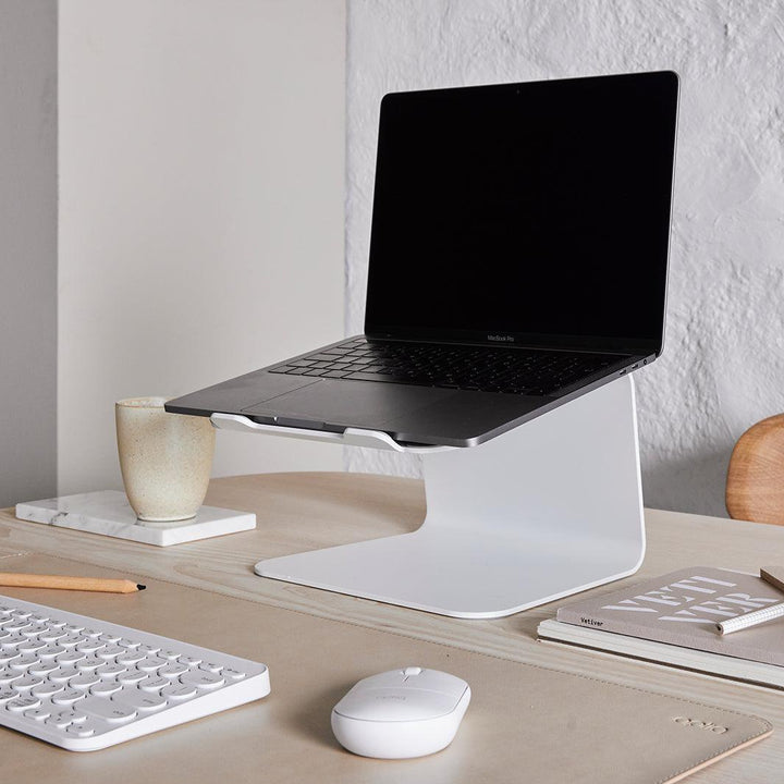 Werkplek met een laptop op een witte standaard met bijpassende accessoires en getoond op een sand kleur bureau onderlegger