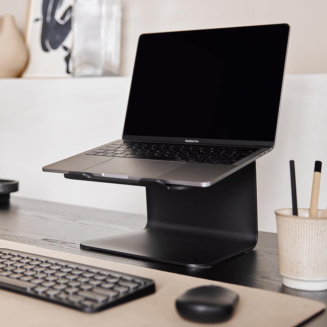 Laptop op een standaard in zwart met bijpassende bureau accessoires op een sand kleur onderlegger