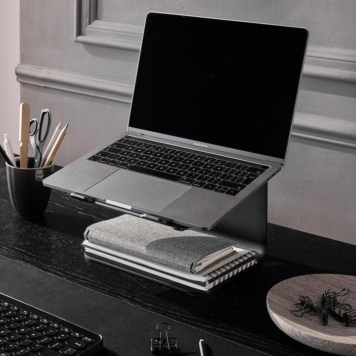 Laptop standaard in zwart met laptop op zwart bureau met accessoires