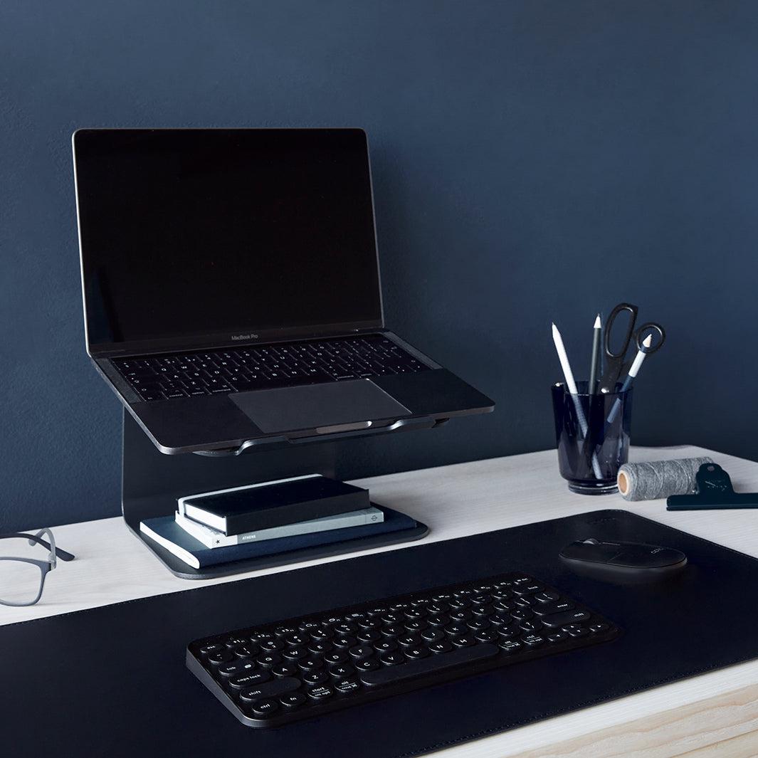 Tegen een donkerblauwe muur gefotografeerd een stijlvolle werkplek met laptop en accessoires in blauw