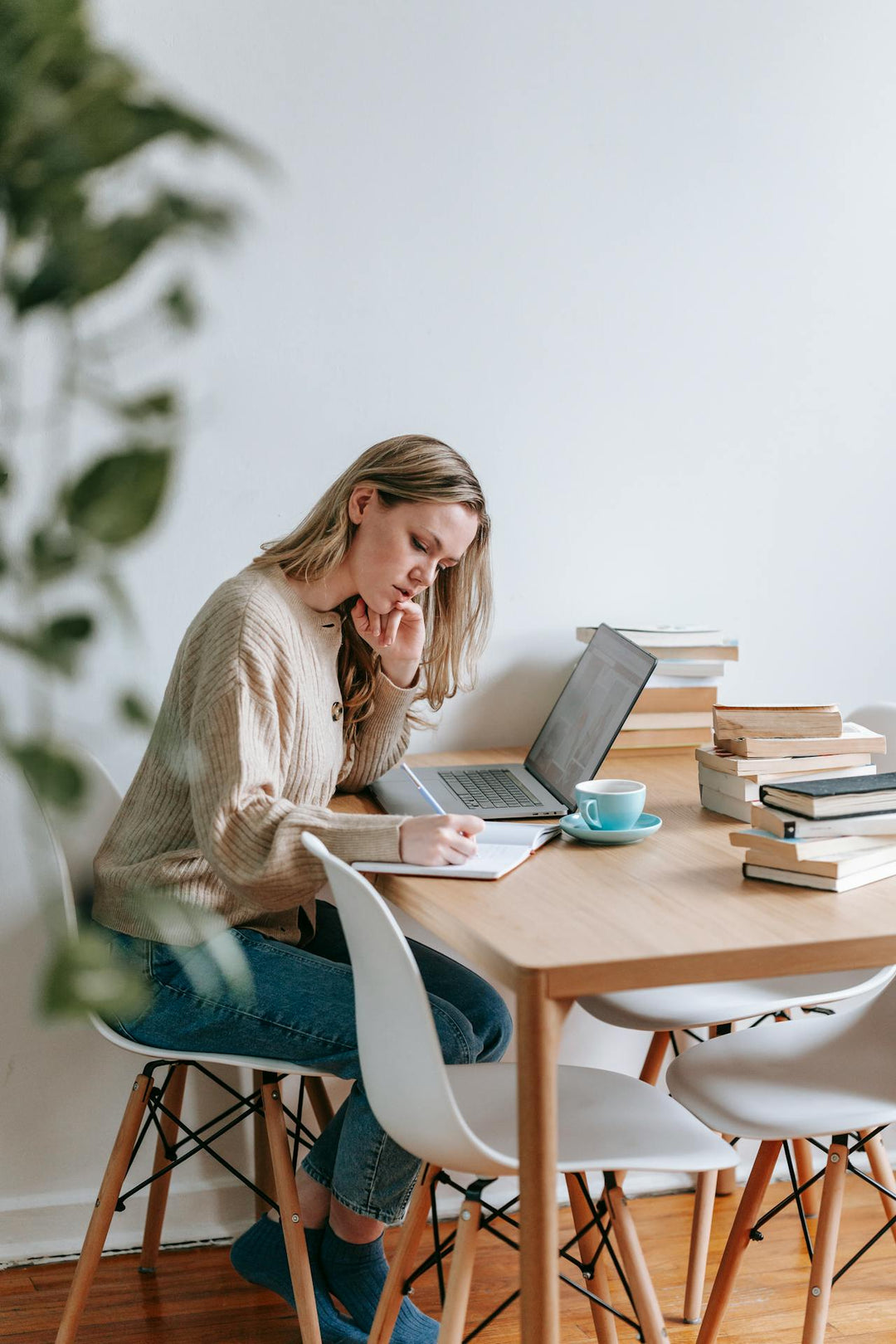 Vrouw werkt thuis aan tafel achter haar laptop en maakt notitie